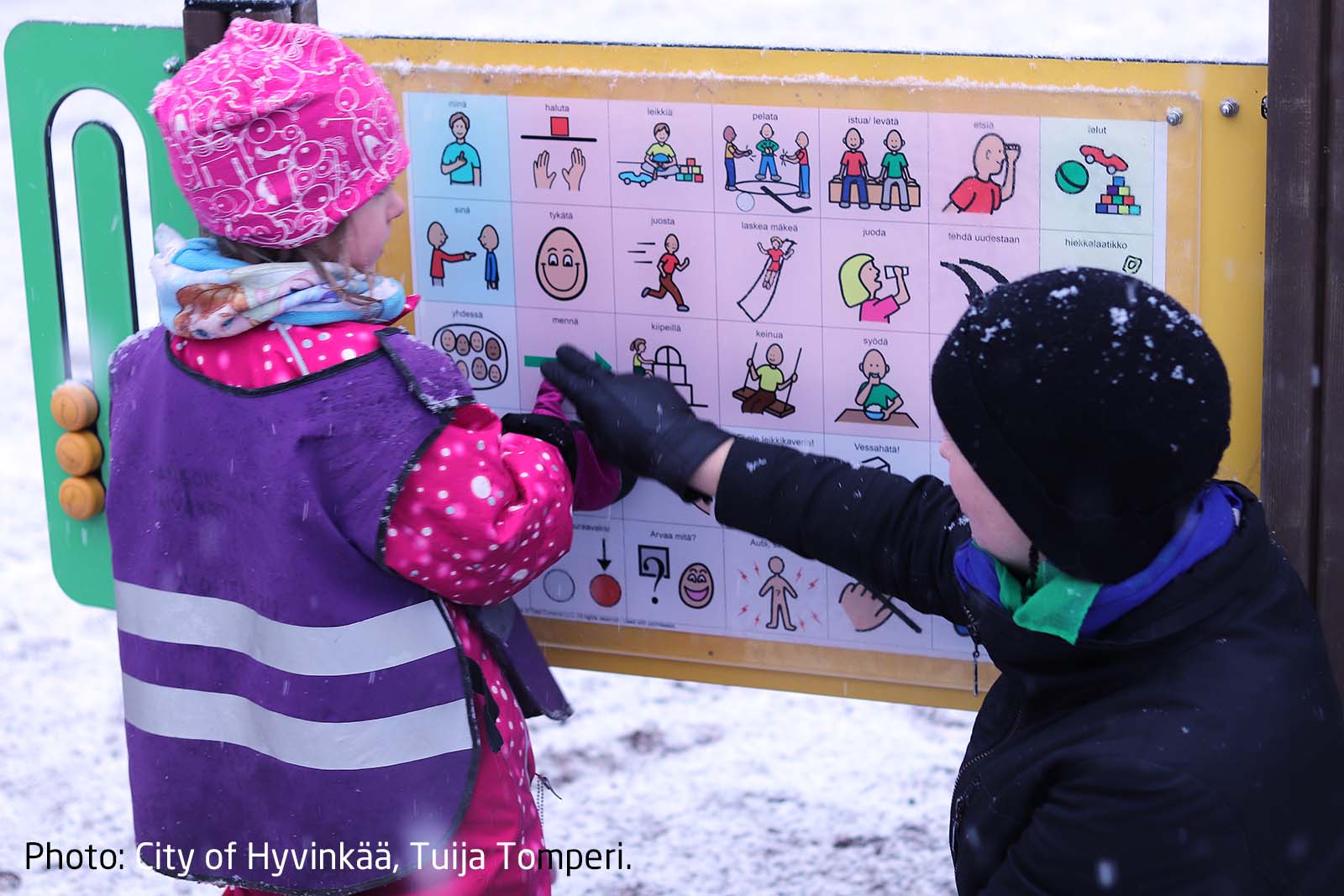 A child with autism pointing to a symbol on a communication board in the playground, expressing their choice.
